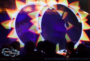 Two performers on stage at Café de Paris spin LED light wands. They display graphics that resemble the sun.