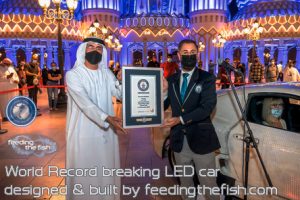 Two men hold a certificate. The text reads World Record breaking LED car designed and built by feeding the fish dot com.