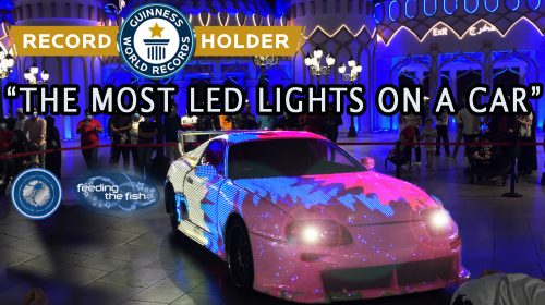 A car covered in LED lights displays graphics in white, blue and pink. Text on the image reads: World record holder. Most LED lights on a Car. Designed and build by Feeding the Fish.