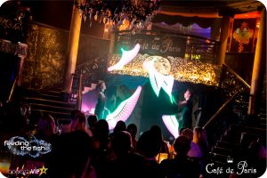 Two performers on stage at Café de Paris spin LED light wands. They display pink and green LED graphics in the air.