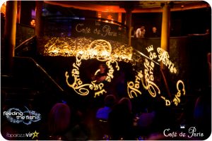 Two performers on stage at Café de Paris spin LED light wands. They display graphics of the Café de Paris logo in the air.